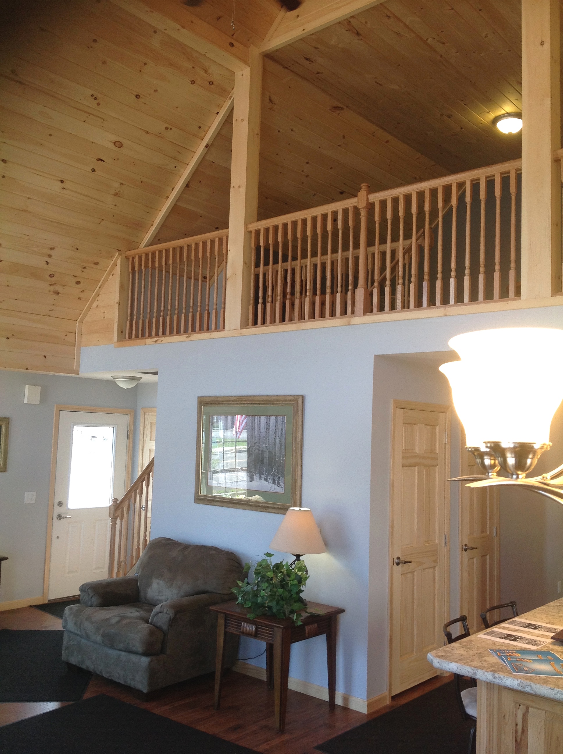 Vaulted loft with pine railing, overlooking living area.